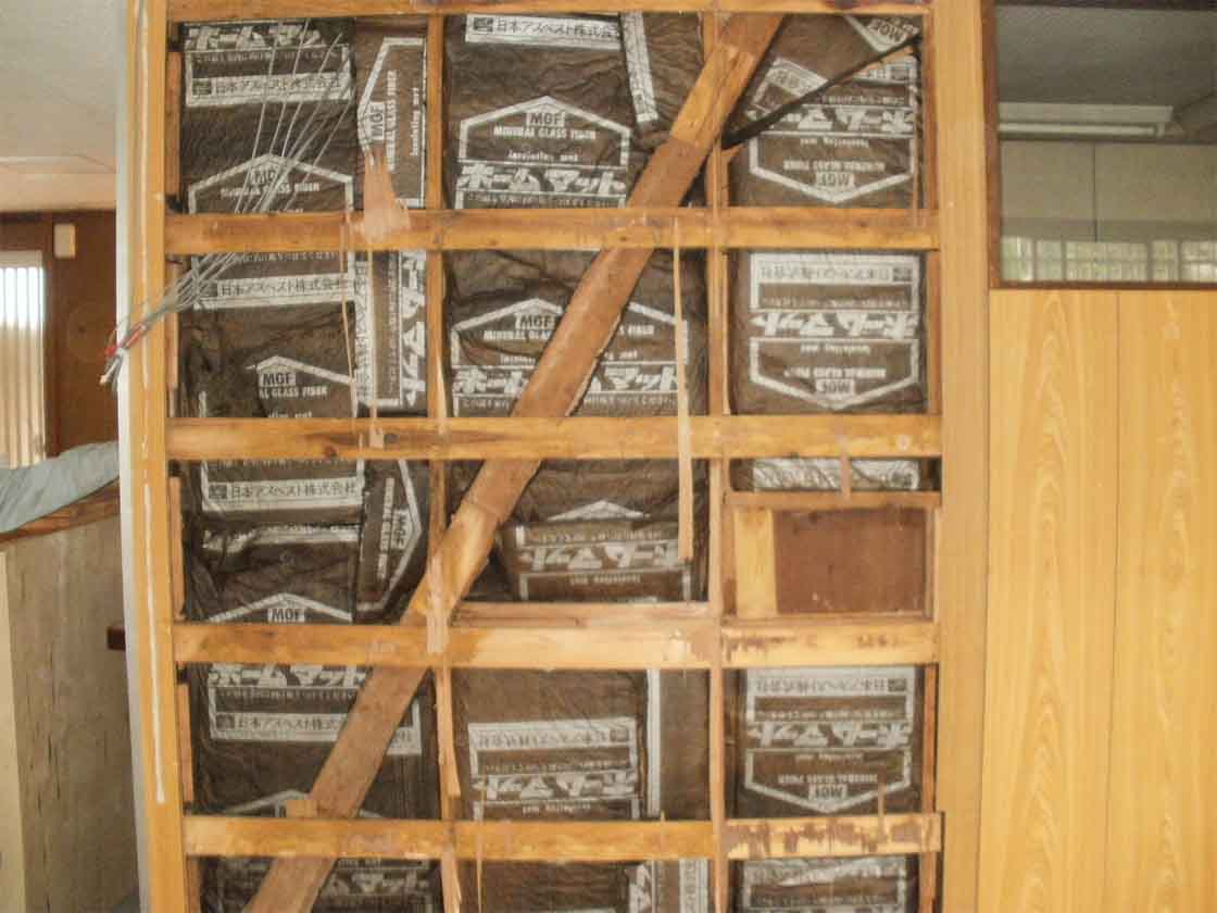 木造住宅の壁面を開口した写真。日本アスベスト株式会社、ホームマットという印字の製品が敷き詰められている